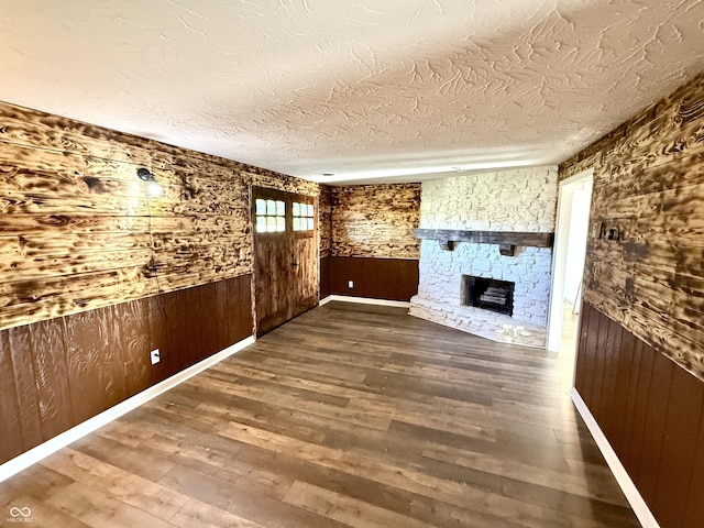 1328 N 300 E, Anderson, IN 46012 - unfurnished living room featuring wooden walls, a textured ceiling, wood finished floors, and a stone fireplace