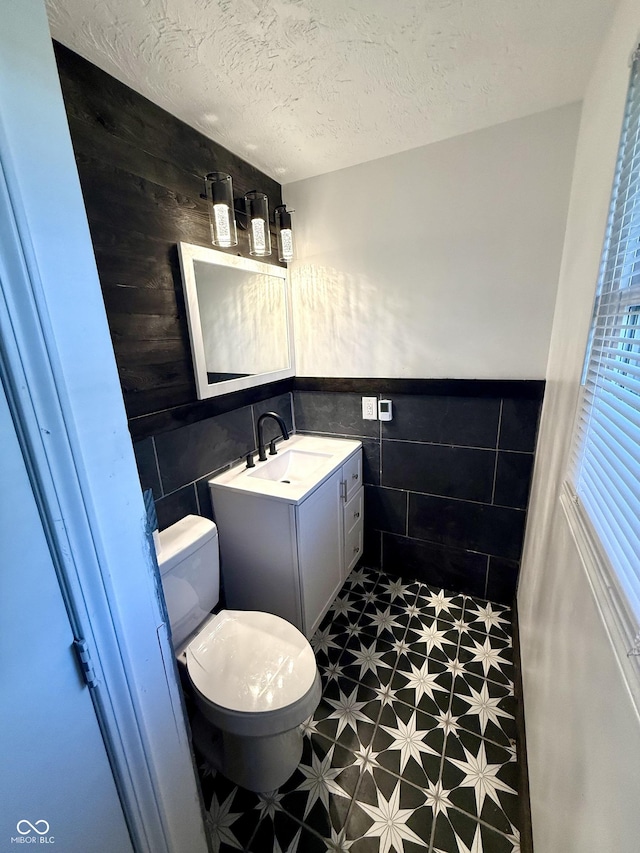 1328 N 300 E, Anderson, IN 46012 - bathroom with tile walls, toilet, vanity, a wainscoted wall, and a textured ceiling