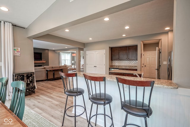 548 Gosford Ct, Westfield, IN 46074 - kitchen with a breakfast bar area, a peninsula, light wood-style floors, dark brown cabinets, and tasteful backsplash
