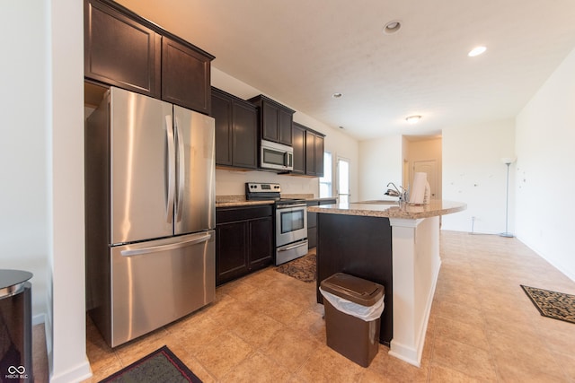 4712 Clairmont Dr, Columbus, IN 47203 - kitchen featuring stainless steel appliances, a sink, a kitchen island with sink, dark brown cabinets, and light stone counters