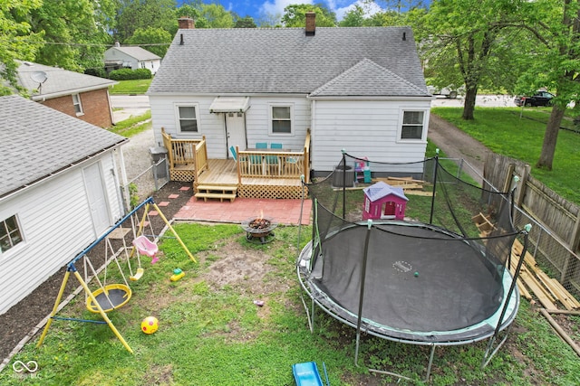 rear view of house featuring a trampoline, a wooden deck, an outdoor fire pit, and a chimney