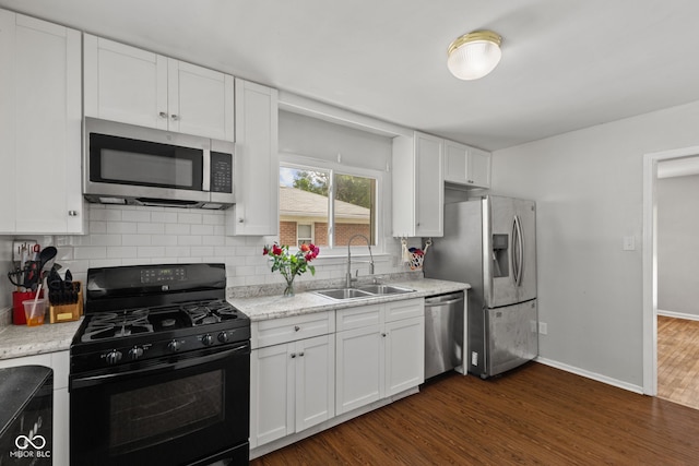 kitchen with appliances with stainless steel finishes, a sink, dark wood finished floors, backsplash, and white cabinetry
