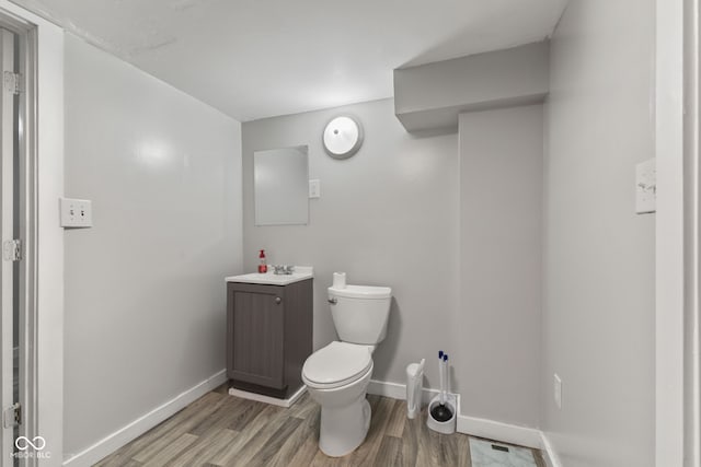 half bathroom featuring toilet, wood finished floors, baseboards, and vanity
