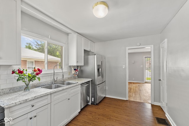 kitchen with a sink, appliances with stainless steel finishes, dark wood finished floors, white cabinetry, and decorative backsplash