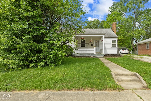 bungalow-style home featuring a chimney, a porch, a front yard, and roof with shingles