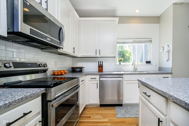 14135 Nicholas Dr, Carmel, IN 46074 - kitchen with appliances with stainless steel finishes, a sink, light wood-style flooring, white cabinets, and decorative backsplash