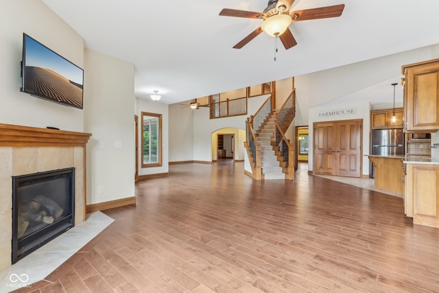 2825 S State Road 267, Plainfield, IN 46168 - unfurnished living room featuring ceiling fan, a tiled fireplace, stairway, arched walkways, and light wood-style floors
