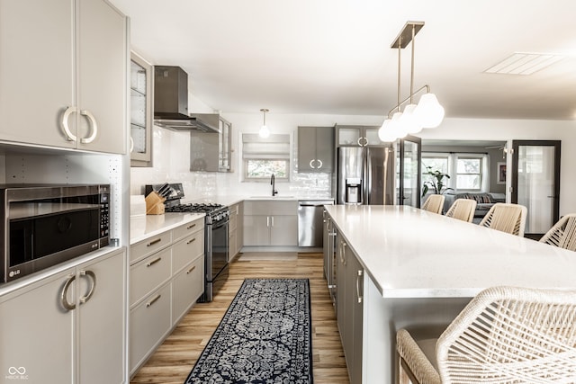 7110 N Layman Ave, Indianapolis, IN 46250 - kitchen with stainless steel appliances, wall chimney range hood, a breakfast bar, gray cabinets, and healthy amount of natural light
