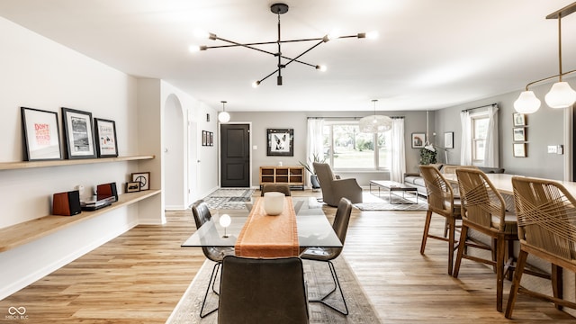 7110 N Layman Ave, Indianapolis, IN 46250 - dining space featuring a chandelier, arched walkways, light wood-style flooring, and baseboards