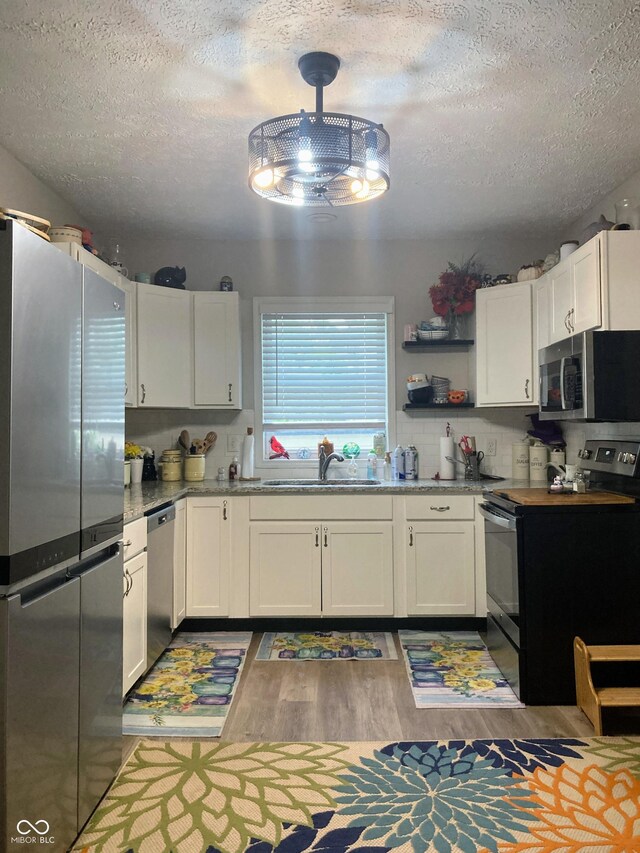 1114 N Olney St, Indianapolis, IN 46201 - kitchen with appliances with stainless steel finishes, a sink, a textured ceiling, light wood-style flooring, and white cabinets