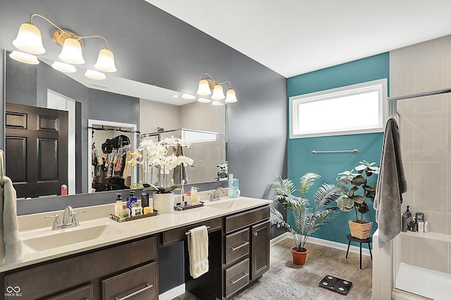 full bathroom featuring a shower with shower door, wood finished floors, double vanity, baseboards, and a walk in closet