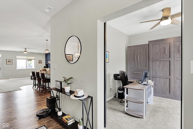 carpeted home office with ceiling fan, baseboards, and wood finished floors