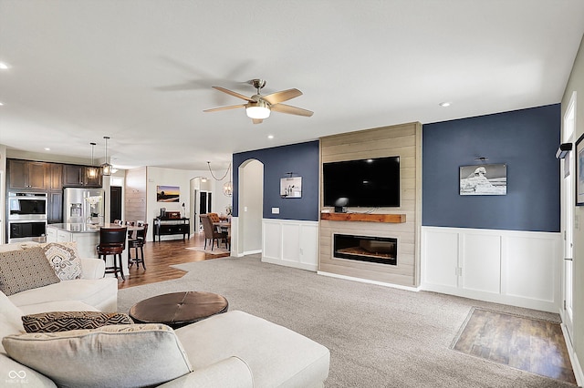 living area with a ceiling fan, recessed lighting, a fireplace, a decorative wall, and a wainscoted wall