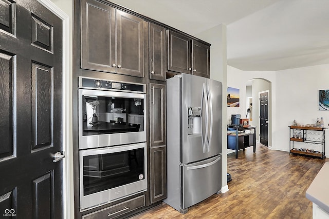 kitchen featuring stainless steel appliances, arched walkways, dark brown cabinetry, and wood finished floors