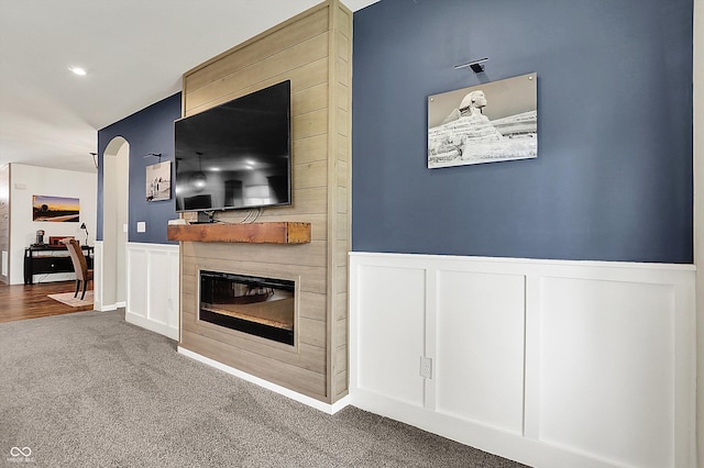 unfurnished living room featuring a decorative wall, carpet floors, a wainscoted wall, a large fireplace, and arched walkways