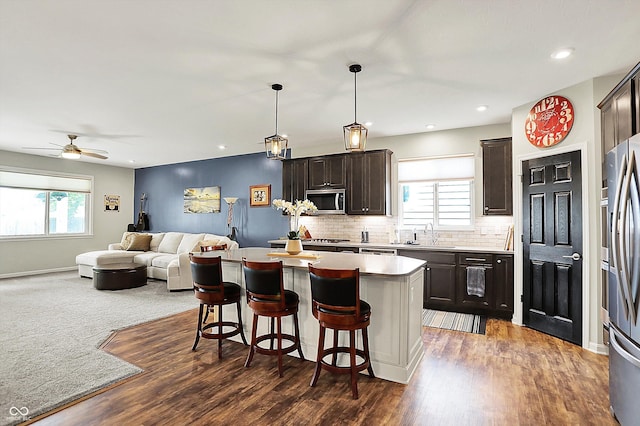 kitchen with stainless steel appliances, open floor plan, dark brown cabinetry, a sink, and a kitchen island