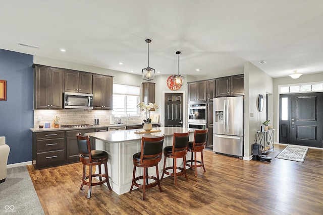 kitchen featuring stainless steel appliances, dark brown cabinetry, dark wood finished floors, a breakfast bar area, and a center island