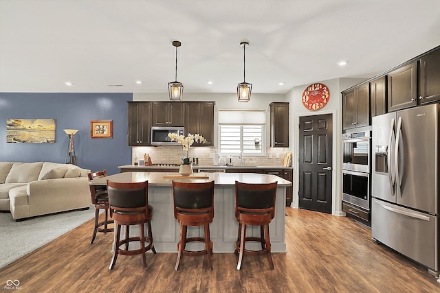 kitchen featuring appliances with stainless steel finishes, open floor plan, dark brown cabinets, a sink, and a kitchen island