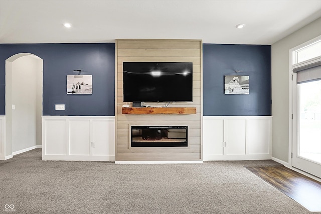 unfurnished living room featuring carpet, a large fireplace, wainscoting, a decorative wall, and arched walkways
