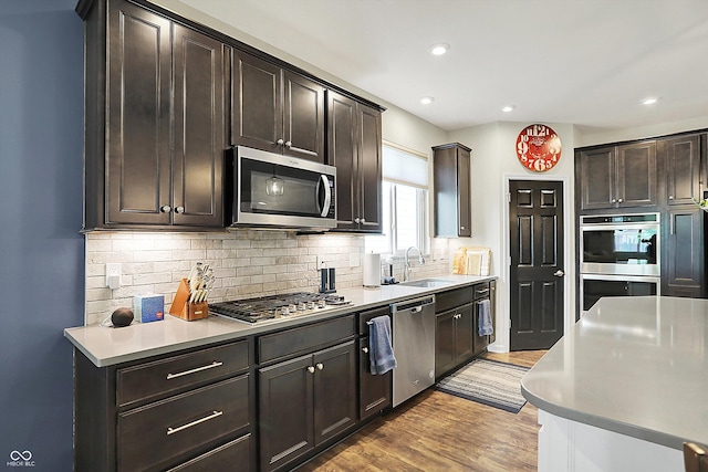 kitchen with appliances with stainless steel finishes, a sink, tasteful backsplash, wood finished floors, and recessed lighting