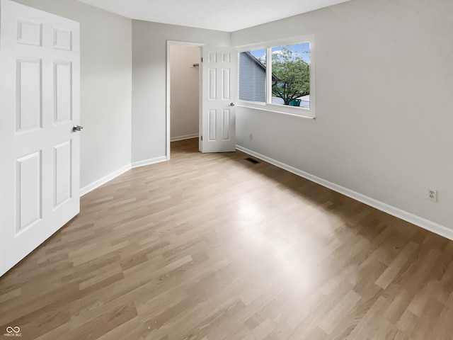 unfurnished bedroom with light wood-style flooring, baseboards, a closet, and a walk in closet