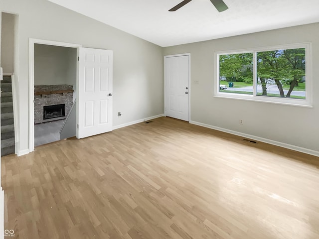 unfurnished living room featuring ceiling fan, light wood-style flooring, baseboards, lofted ceiling, and a fireplace