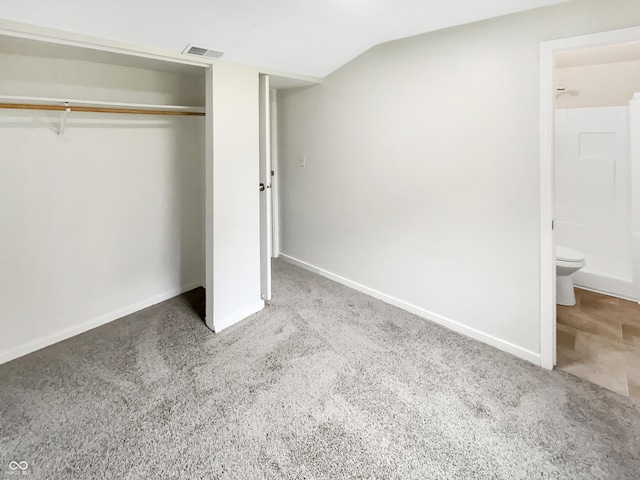 unfurnished bedroom with a closet, carpet floors, baseboards, vaulted ceiling, and ensuite bathroom
