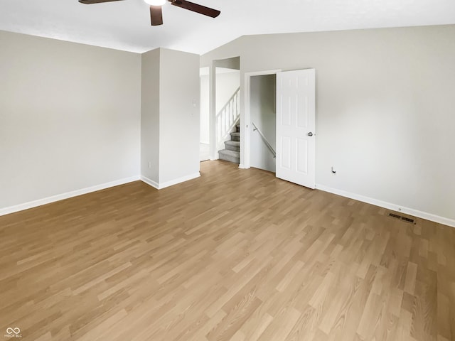 unfurnished room featuring a ceiling fan, baseboards, wood finished floors, vaulted ceiling, and stairs