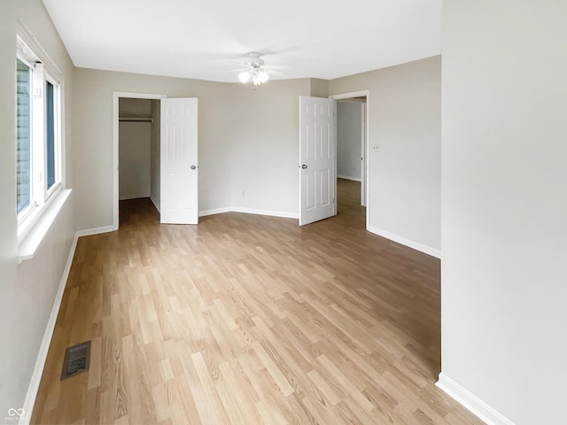 unfurnished bedroom featuring light wood finished floors, baseboards, and a spacious closet