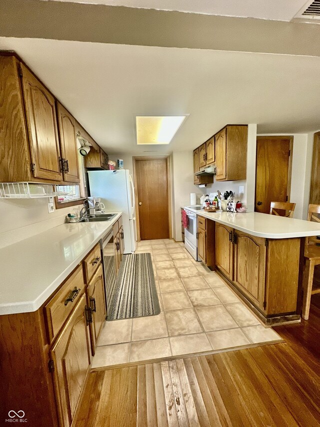 1154 W US Highway 136, Veedersburg, IN 47987 - kitchen with white appliances, brown cabinetry, a peninsula, under cabinet range hood, and light countertops