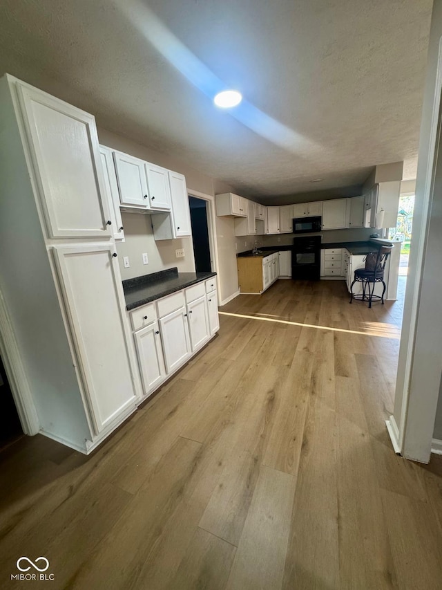 2931 Byrkit St, Indianapolis, IN 46217 - kitchen with black appliances, wood finished floors, dark countertops, and white cabinetry