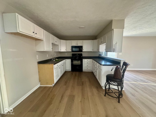 2931 Byrkit St, Indianapolis, IN 46217 - kitchen with black appliances, a textured ceiling, light wood-type flooring, dark countertops, and white cabinets