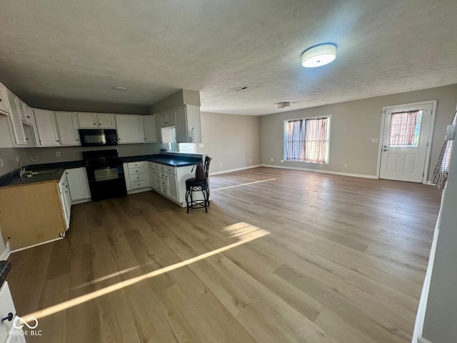 2931 Byrkit St, Indianapolis, IN 46217 - kitchen with black appliances, dark countertops, wood finished floors, open floor plan, and a textured ceiling