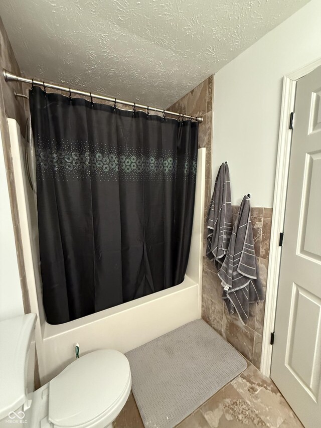 9535 Longwell Dr, Indianapolis, IN 46240 - bathroom featuring shower / tub combo, toilet, a textured ceiling, tile walls, and wainscoting