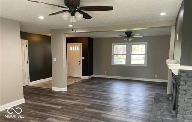 7731 Scarborough Blvd S, Indianapolis, IN 46256 - unfurnished living room featuring a ceiling fan, baseboards, dark wood-style floors, recessed lighting, and a fireplace with raised hearth
