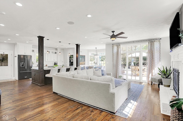 3398 Nottinghill Blvd, Plainfield, IN 46168 - living room featuring a ceiling fan, dark wood finished floors, recessed lighting, a fireplace with raised hearth, and decorative columns