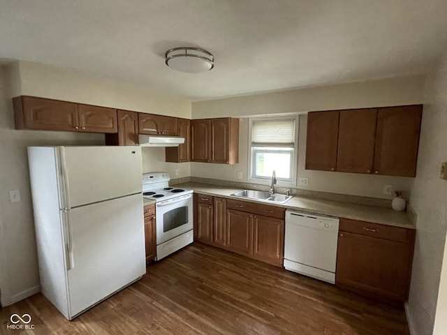 kitchen with white appliances, a sink, under cabinet range hood, dark wood-type flooring, and light countertops