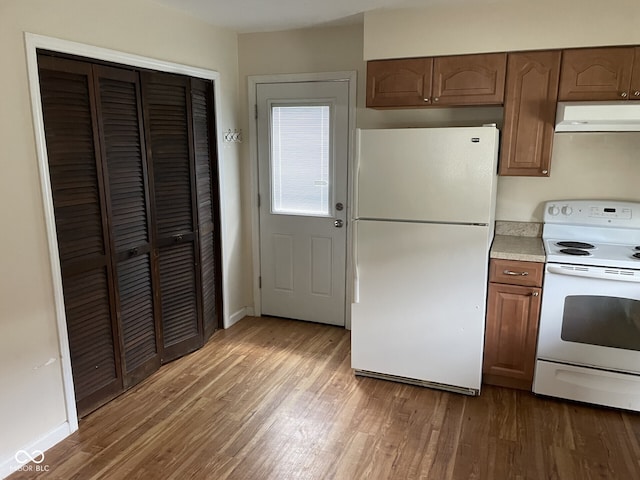 kitchen featuring white appliances, under cabinet range hood, wood finished floors, and light countertops
