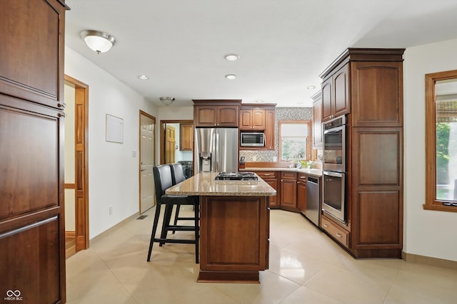 12335 Old Stone Dr, Indianapolis, IN 46236 - kitchen featuring stainless steel appliances, a kitchen island, a breakfast bar, decorative backsplash, and light stone counters