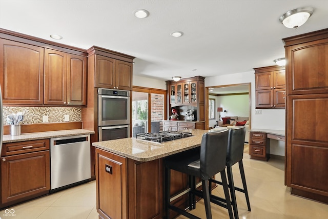 12335 Old Stone Dr, Indianapolis, IN 46236 - kitchen with appliances with stainless steel finishes, a kitchen breakfast bar, light stone counters, backsplash, and a center island