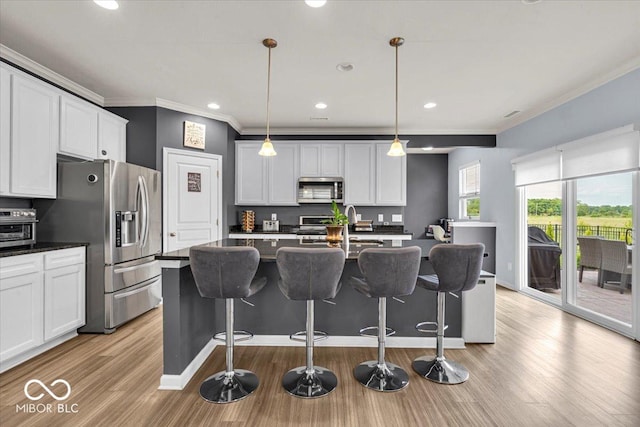 13495 Forest Glade Dr, Fishers, IN 46037 - kitchen with stainless steel appliances, dark countertops, crown molding, light wood finished floors, and a kitchen breakfast bar