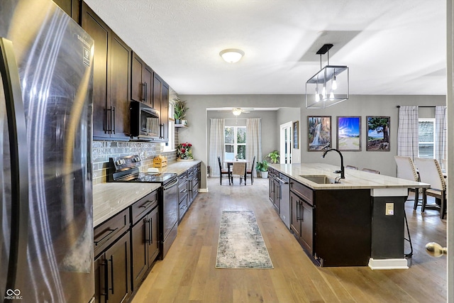 1664 Woodside Cir, Franklin, IN 46131 - kitchen featuring appliances with stainless steel finishes, dark brown cabinetry, backsplash, light wood-style flooring, and an island with sink