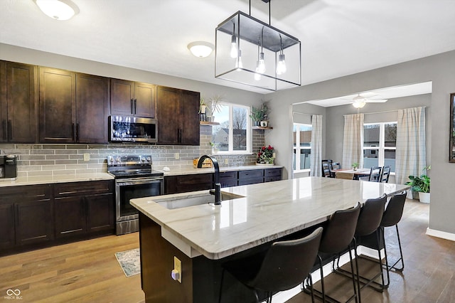 1664 Woodside Cir, Franklin, IN 46131 - kitchen featuring appliances with stainless steel finishes, a breakfast bar area, open shelves, decorative backsplash, and light wood finished floors
