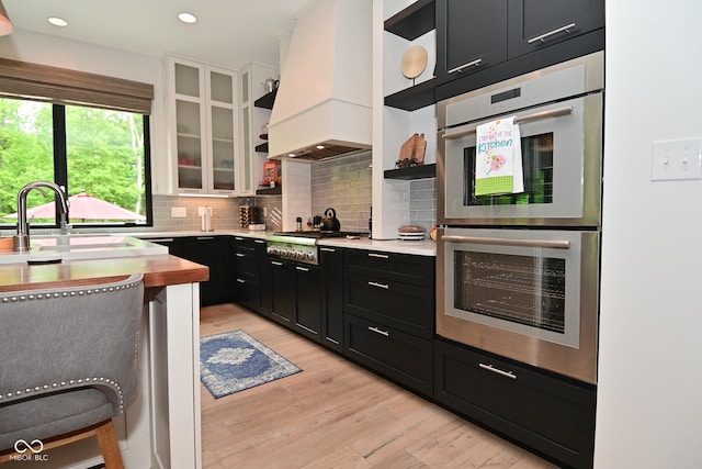 7070 Dean Rd, Indianapolis, IN 46220 - kitchen with appliances with stainless steel finishes, premium range hood, dark cabinets, open shelves, and light wood-style flooring