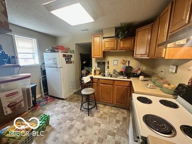 162 N Gladstone Ave, Columbus, IN 47201 - kitchen with white appliances, under cabinet range hood, light countertops, a textured ceiling, and brown cabinetry