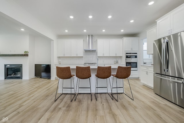 1510 Stonehaven Dr, Westfield, IN 46074 - kitchen featuring stainless steel appliances, wall chimney range hood, a kitchen island with sink, decorative backsplash, and light wood-style floors