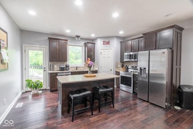 121 George Ct, Danville, IN 46122 - kitchen featuring appliances with stainless steel finishes, a kitchen island, dark brown cabinets, dark wood-type flooring, and decorative backsplash
