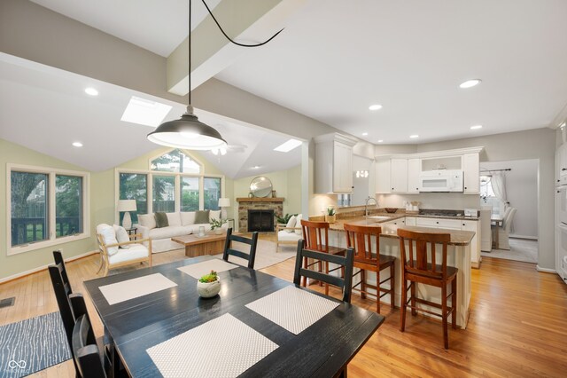6020 Gladden Dr, Indianapolis, IN 46220 - dining space with a stone fireplace, a skylight, light wood-style floors, vaulted ceiling, and recessed lighting