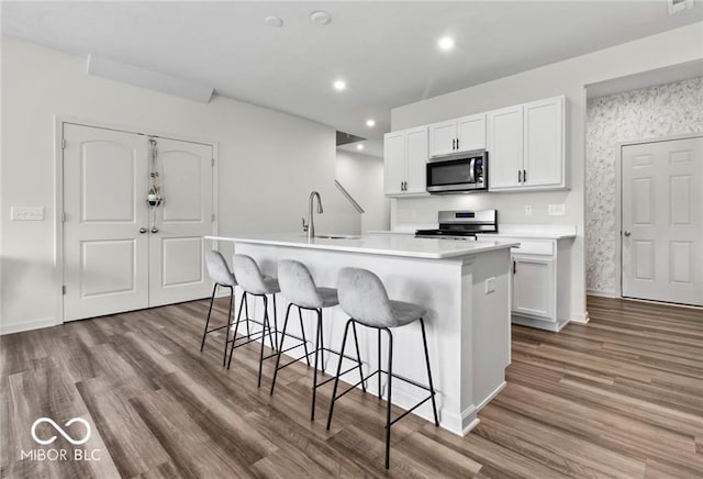 14350 Ludwell Ct, Fishers, IN 46037 - kitchen with appliances with stainless steel finishes, a sink, a kitchen island with sink, white cabinetry, and wood finished floors