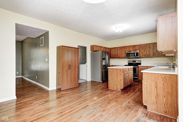1306 Flat Wood Ct, Brownsburg, IN 46112 - kitchen with stainless steel appliances, light wood-style flooring, a center island, light countertops, and washer / clothes dryer